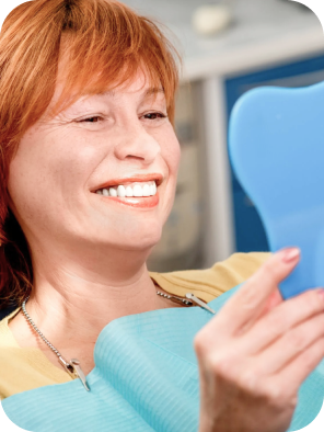 Smiling senior woman with new dental implants sitting in the dental office and looking at the mirror