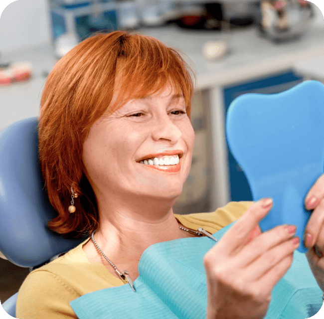 Smiling woman with new dental implants and looking at the mirror